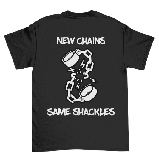 The image is of a black T-shirt featuring a design on the back. The design includes an illustration of broken shackles with lightning bolts around the break, symbolizing a sense of breaking free or resistance. The text above and below the illustration reads: “New Chains, Same Shackles”