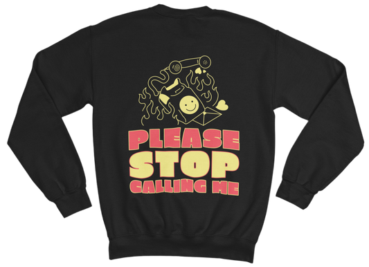 The image shows a black sweatshirt with a graphic design on the back. The design features a burning old-school phone with a smiley face on its screen, a detached phone receiver, and small heart shapes around it. Below the illustration, bold, retro-style text in red and yellow reads: “PLEASE STOP CALLING ME”
